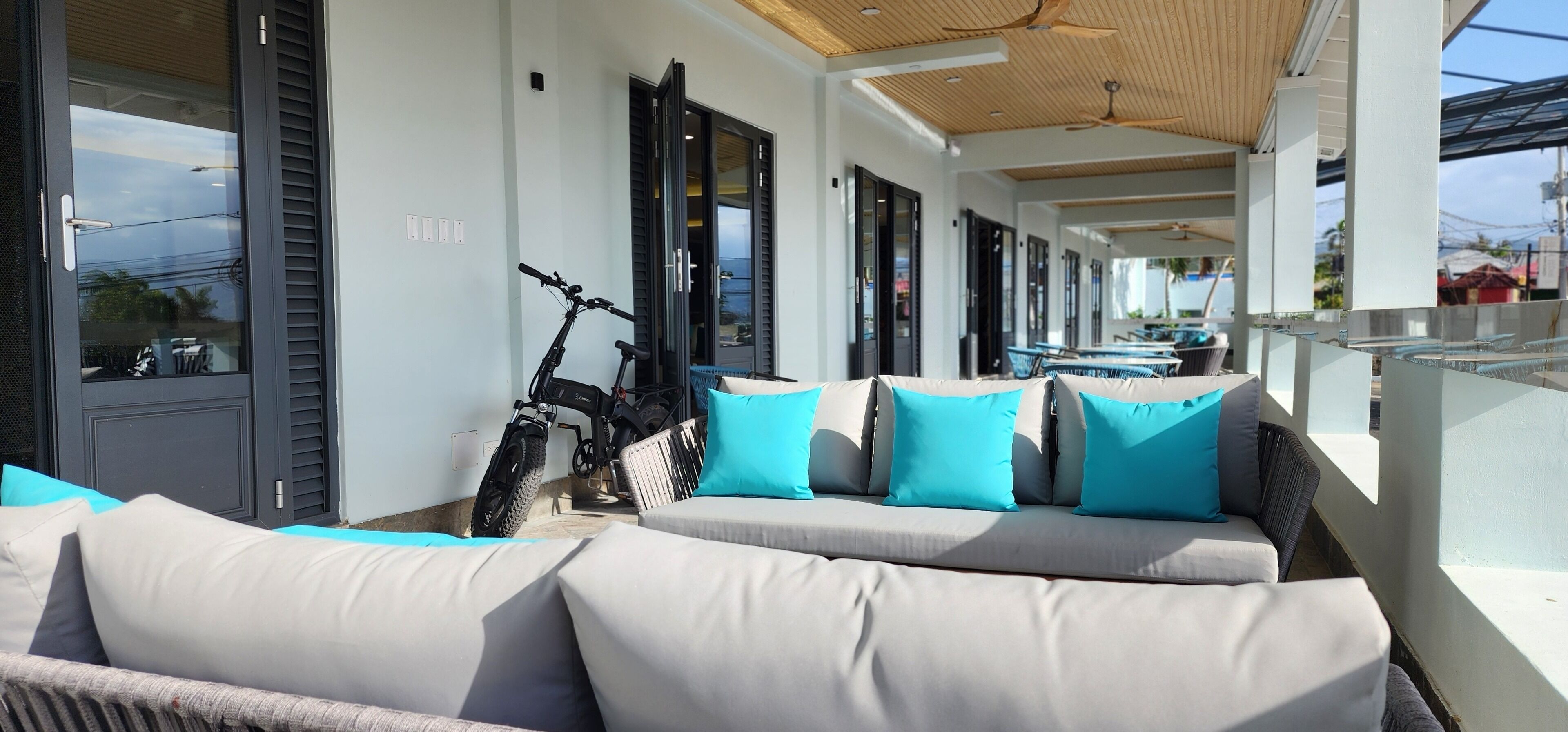 A covered outdoor seating area with a sofa and cushions, a bicycle, and a pool in the background.