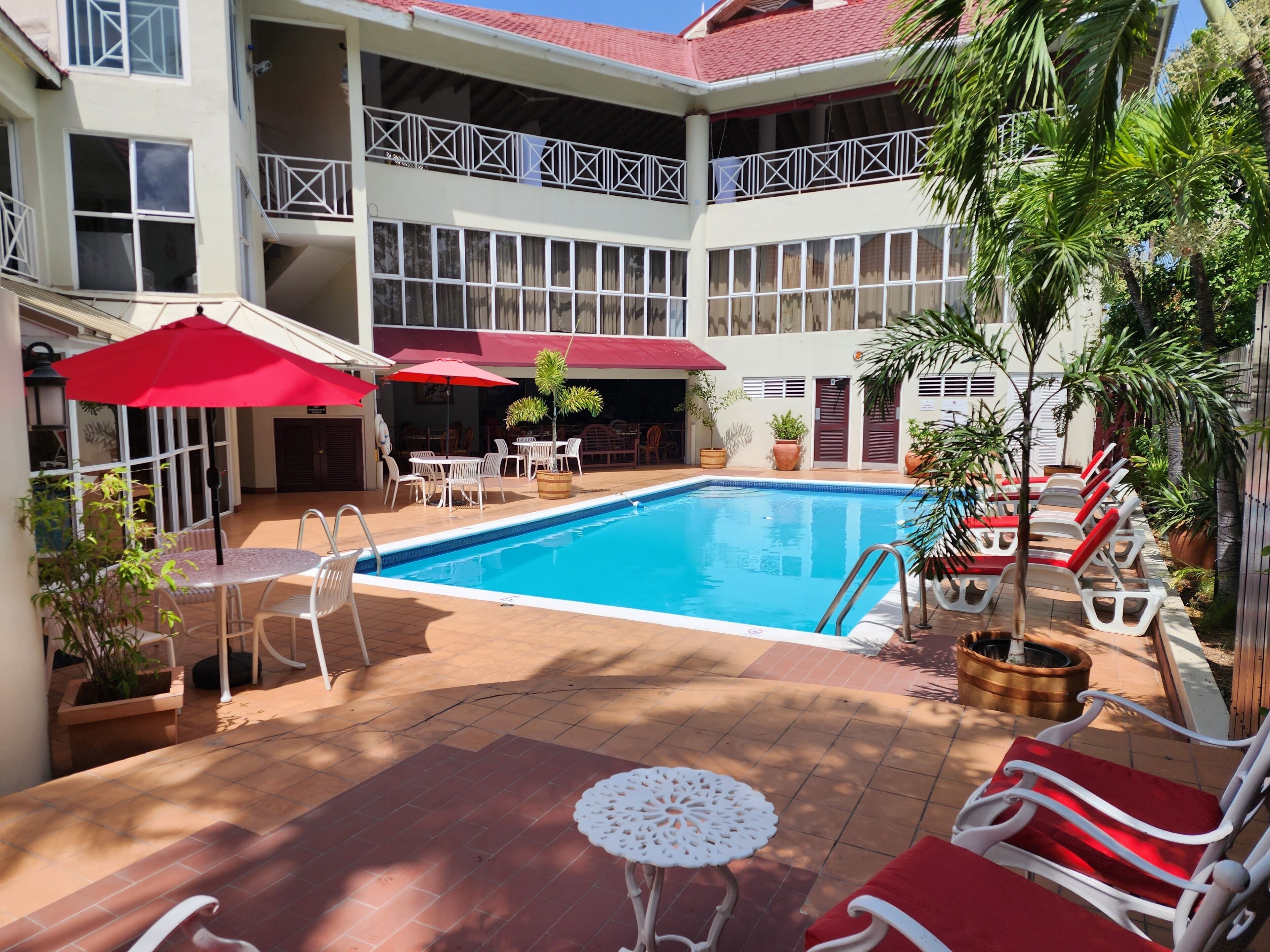 A swimming pool with lounge chairs and umbrellas, surrounded by a building with multiple floors and balconies.