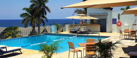 Una piscina al aire libre, sombrillas, sillones reclinables de piscina