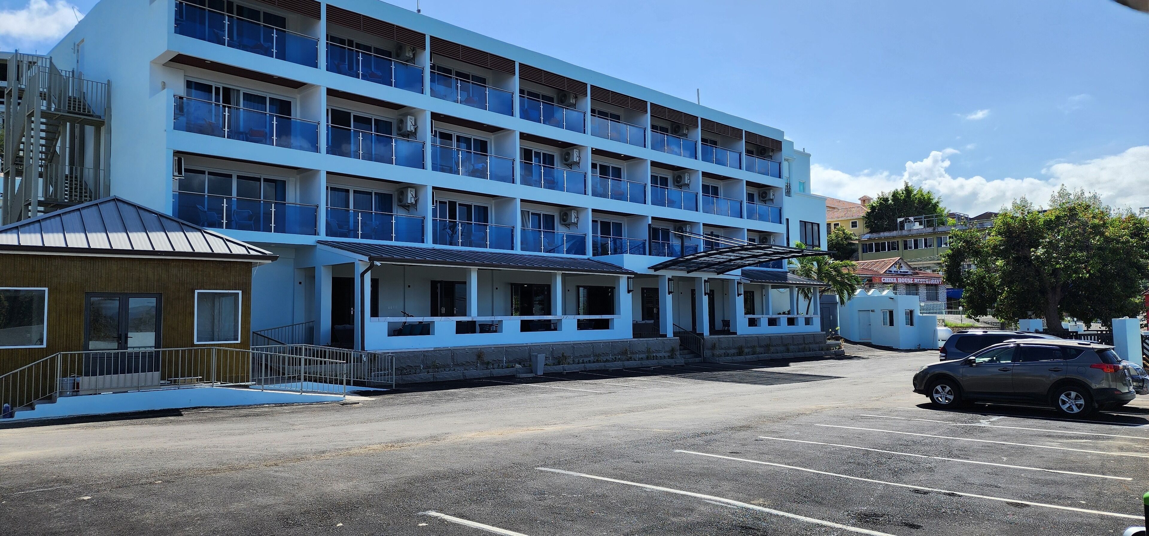 Ein mehrgeschossiges Hotel mit blauer Fassade, einer überdachten Eingangsparte und einem Parkplatz mit Autos.