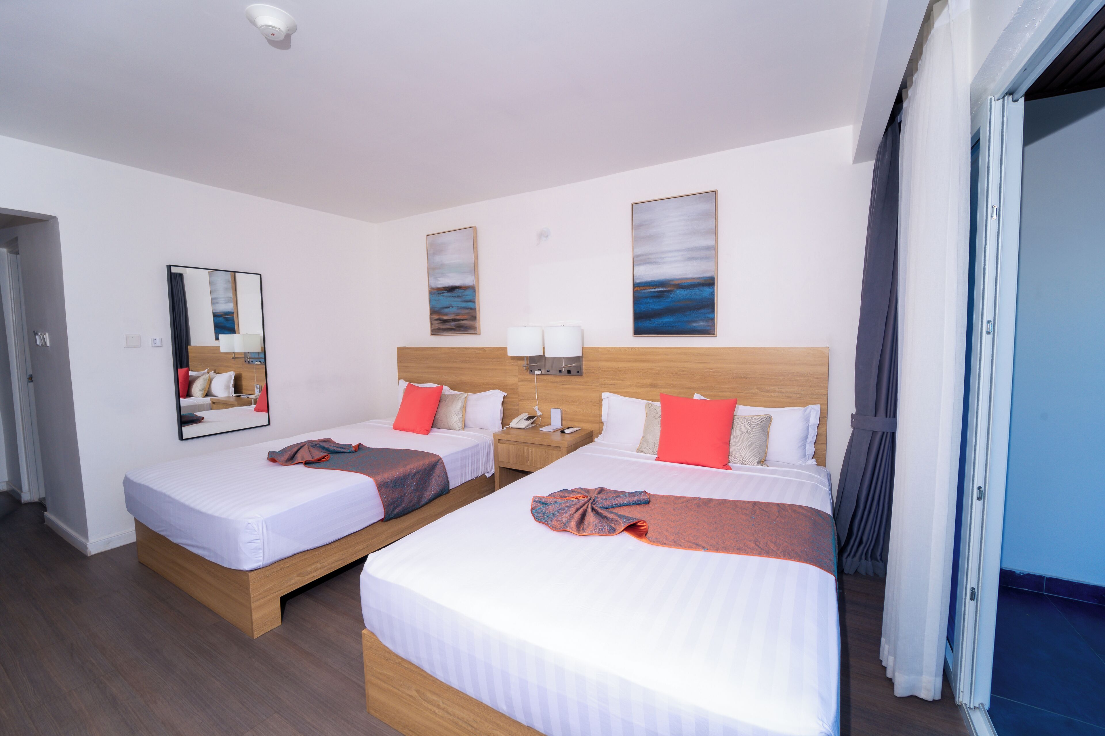 Une chambre d’hôtel avec deux lits, une tête de lit en bois, une table de chevet avec un téléphone et une fenêtre avec des rideaux.
