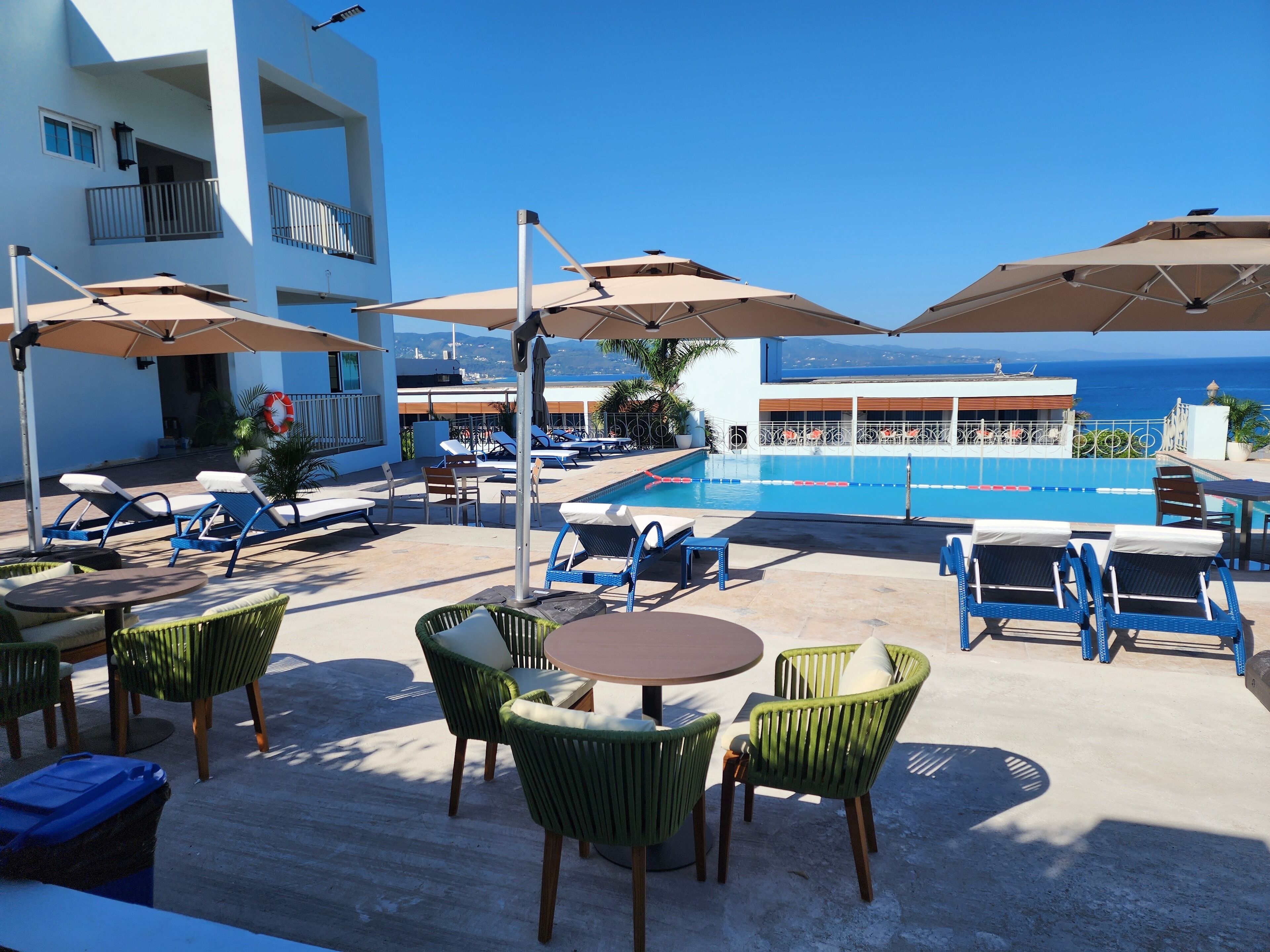 Un espace aménagé au bord de la piscine, avec des chaises longues, des parasols et une vue sur la mer.