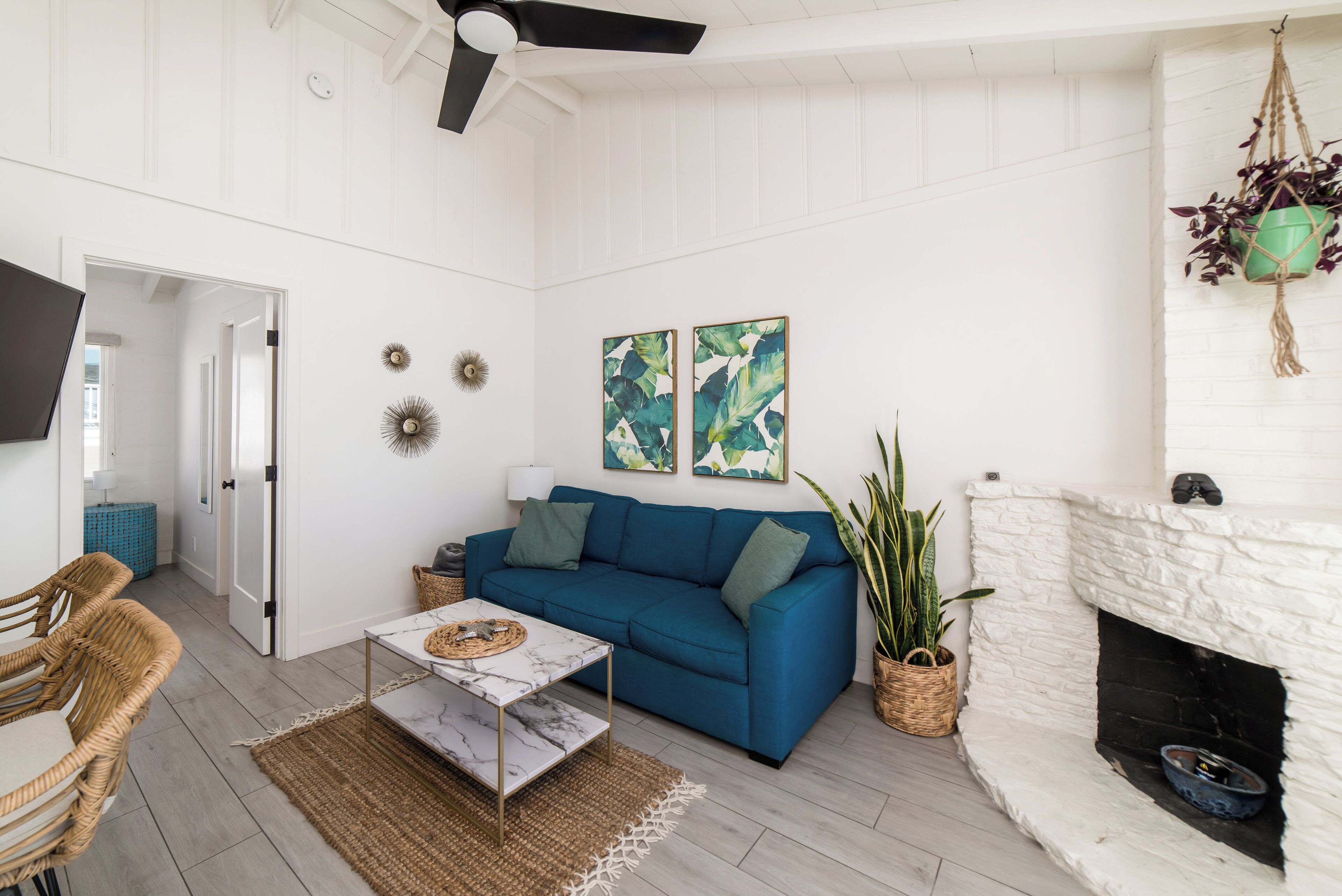 A living room with a blue sofa, white fireplace, and a ceiling fan.