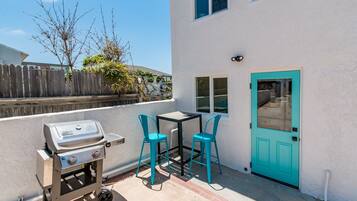 A patio with a grill, two chairs, and a table.