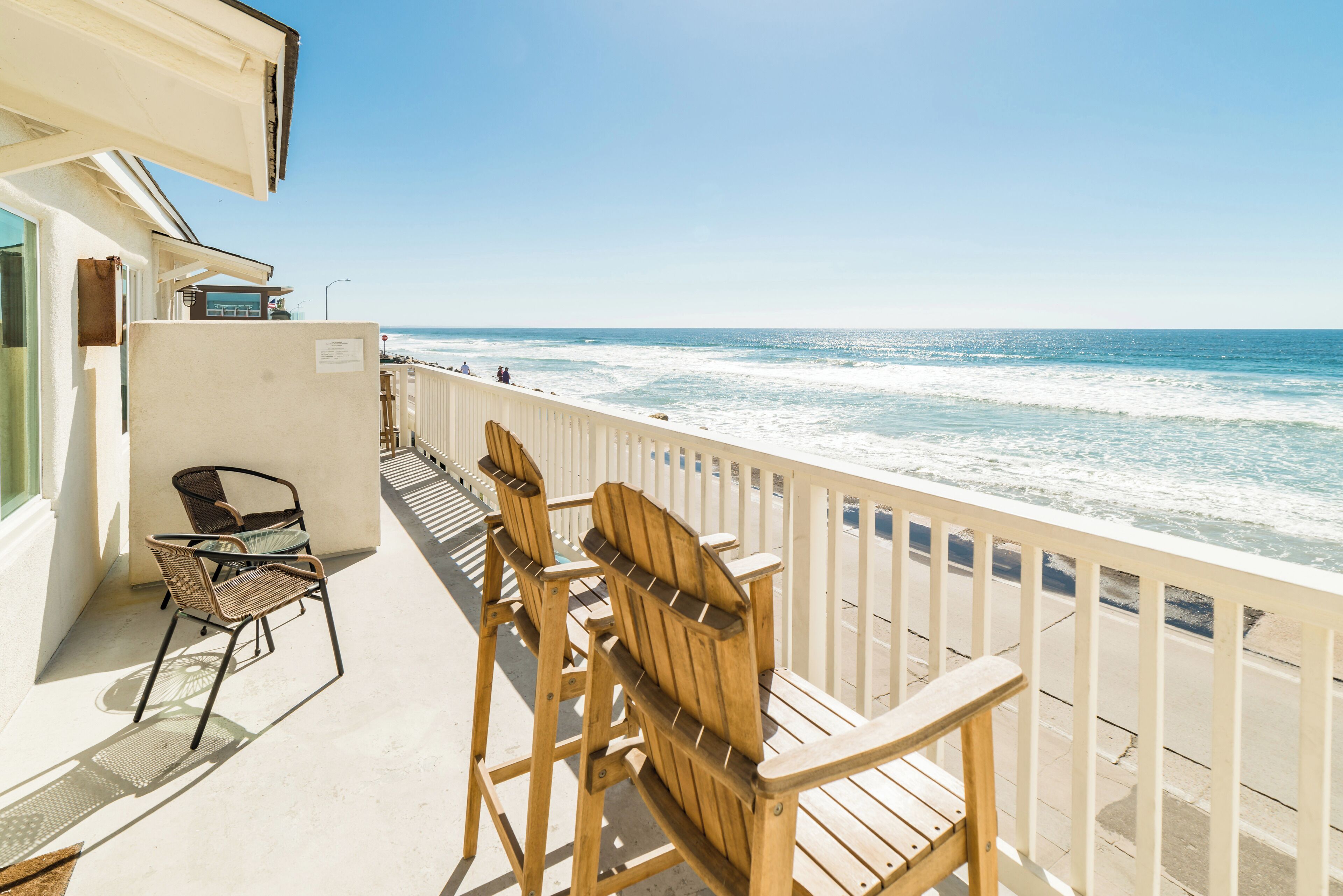 A balcony with wooden chairs and a table overlooking the beach.