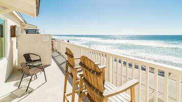 Un balcon avec des chaises et une table en bois, donnant sur la plage.