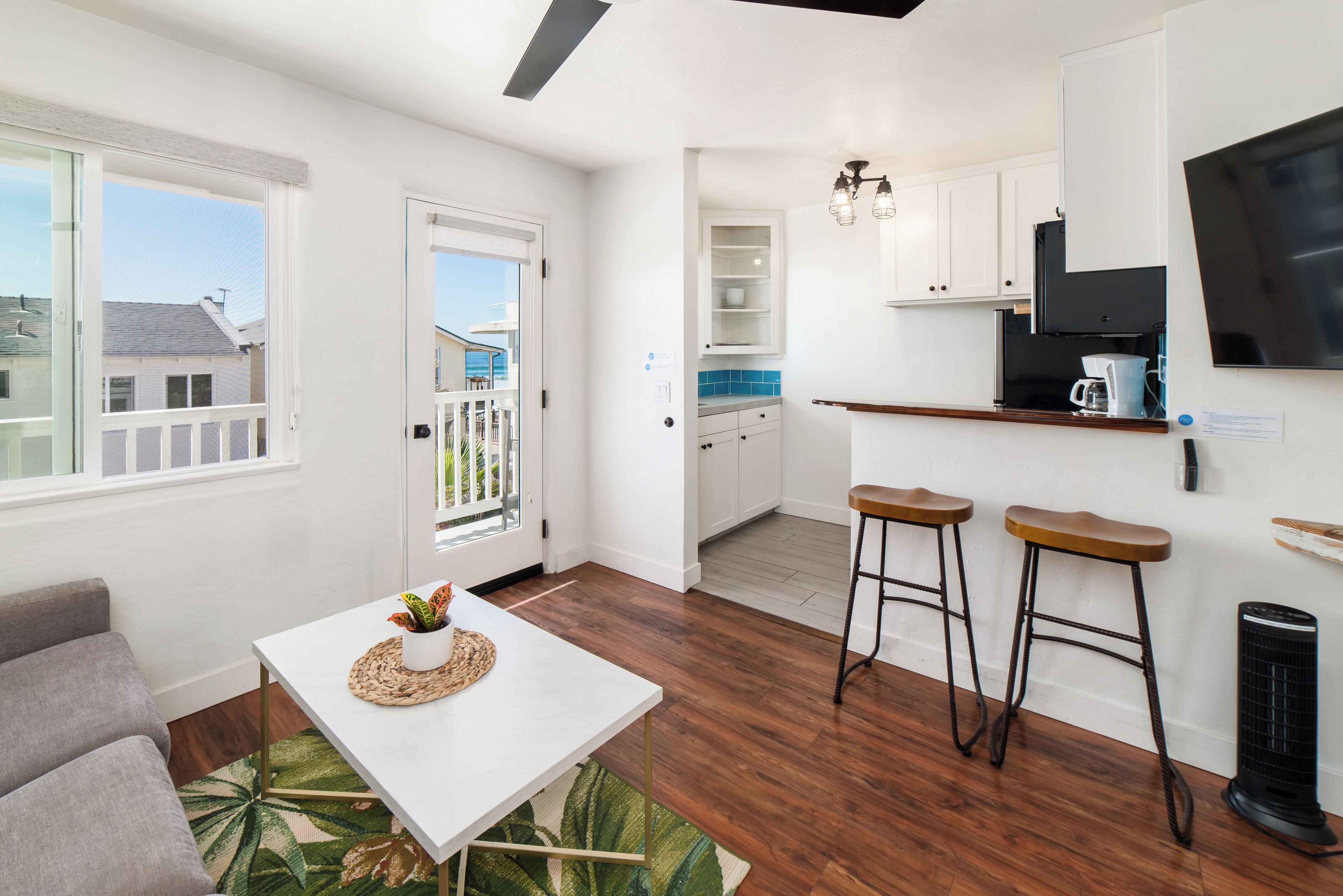 Una cocina moderna con armarios blancos, una campana extractora negra y un comedor con una mesa blanca y dos taburetes de bar.