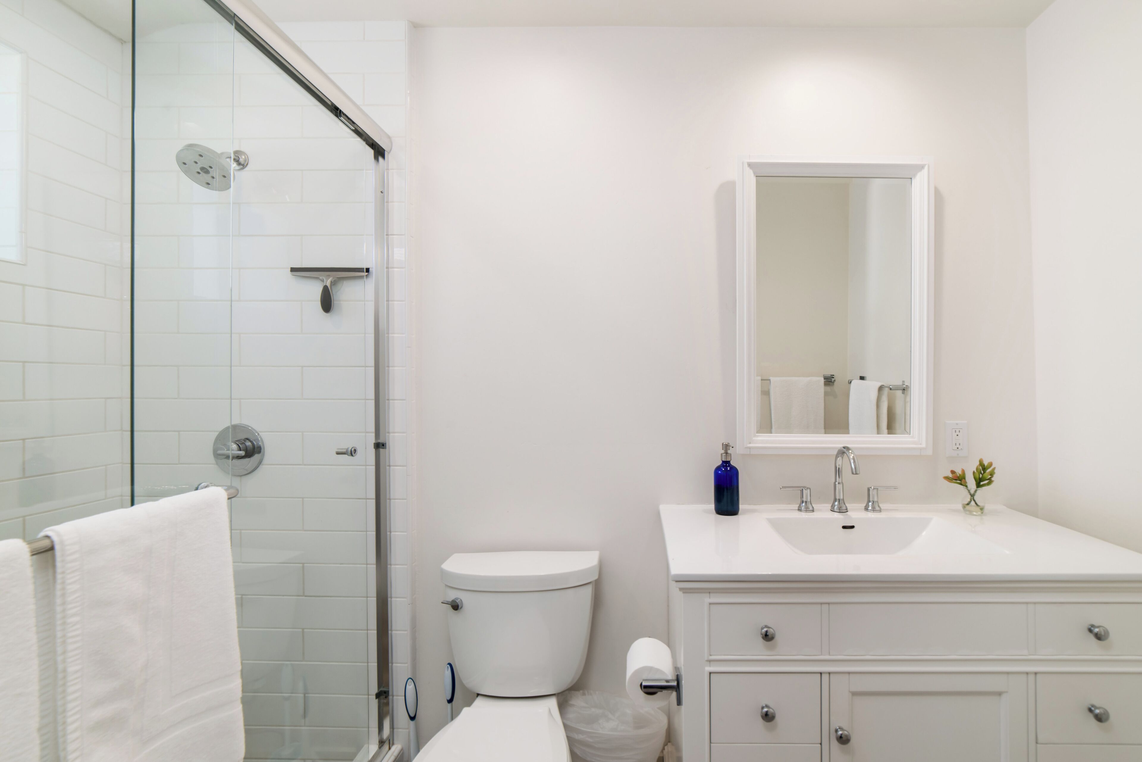 A modern bathroom with a glass shower enclosure, a white toilet, a sink with a mirror, and a white towel hanging on a rack.