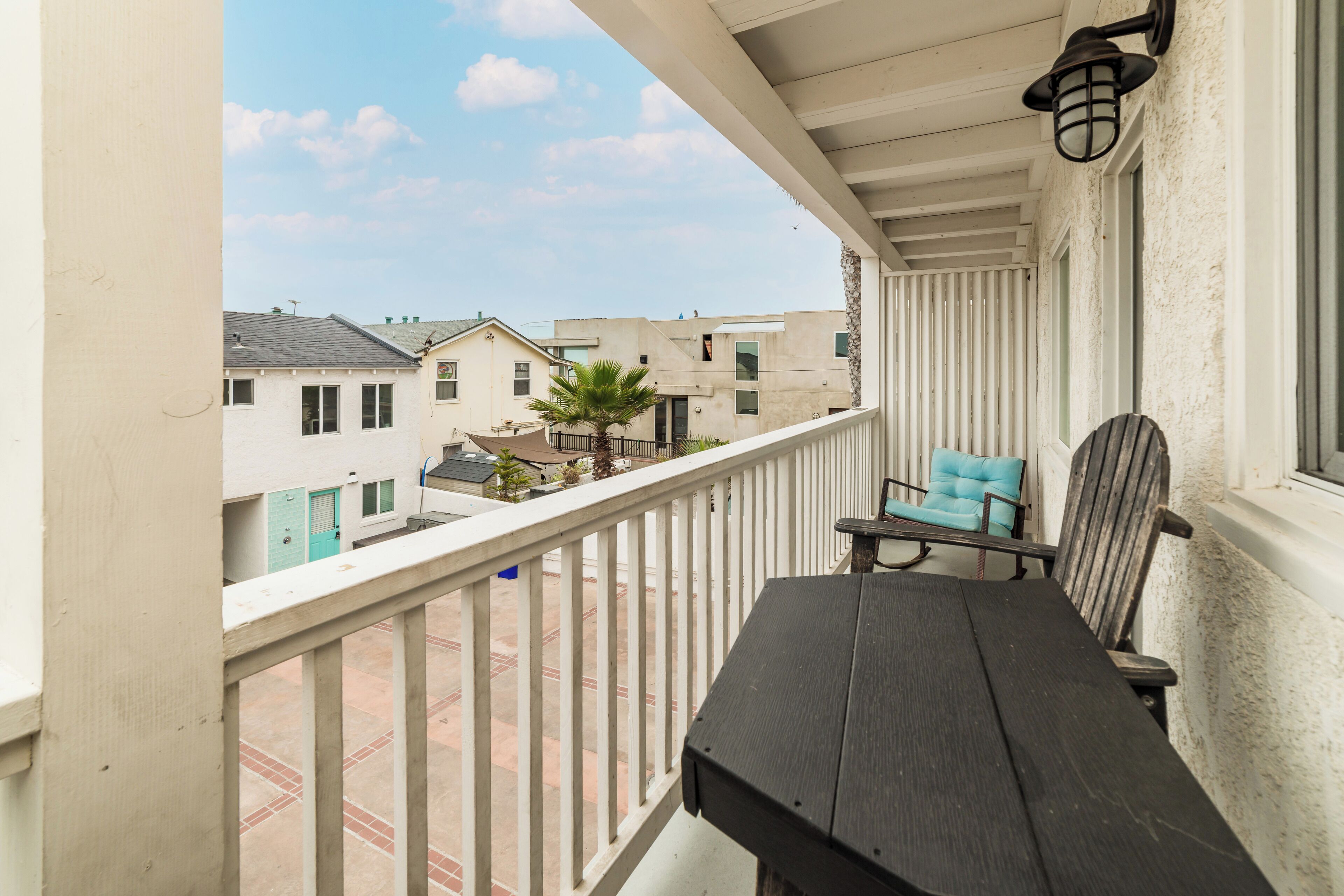 A balcony with a table and chairs, a view of neighboring buildings, and a clear sky.