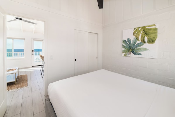 Un dormitorio con cama, una puerta y vista al océano a través de una ventana.