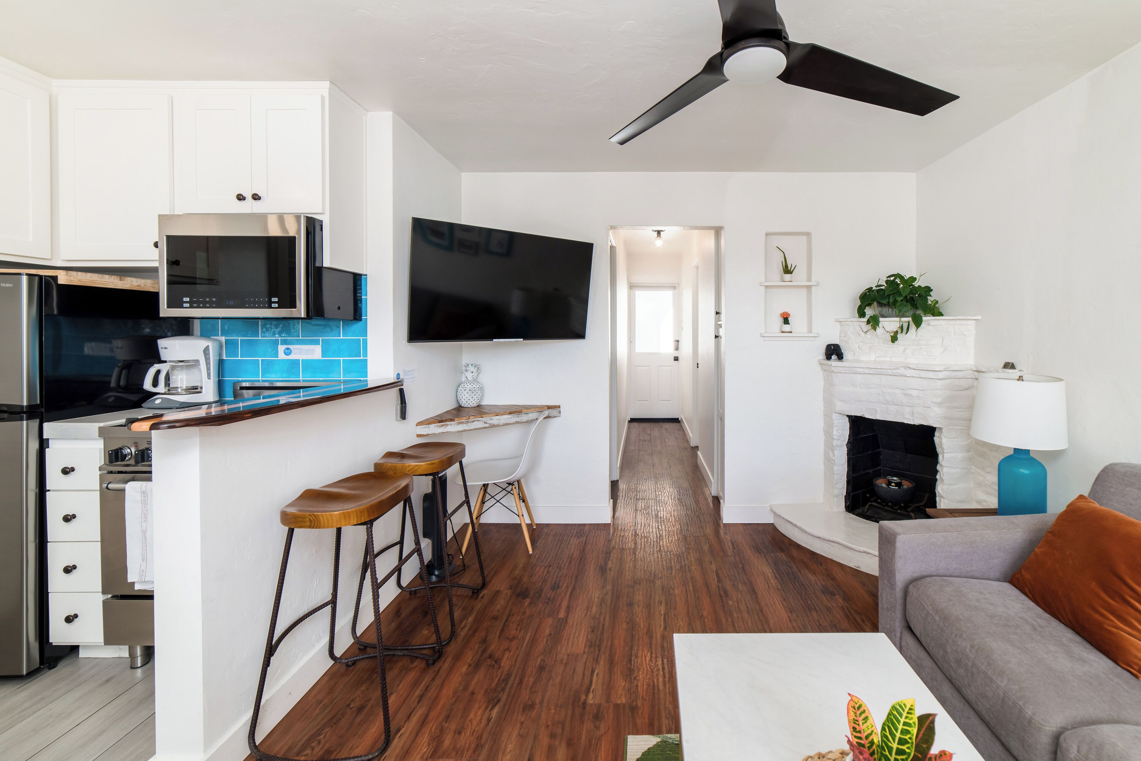 A modern kitchen with white cabinets, a stainless steel microwave, and a flat-screen TV.