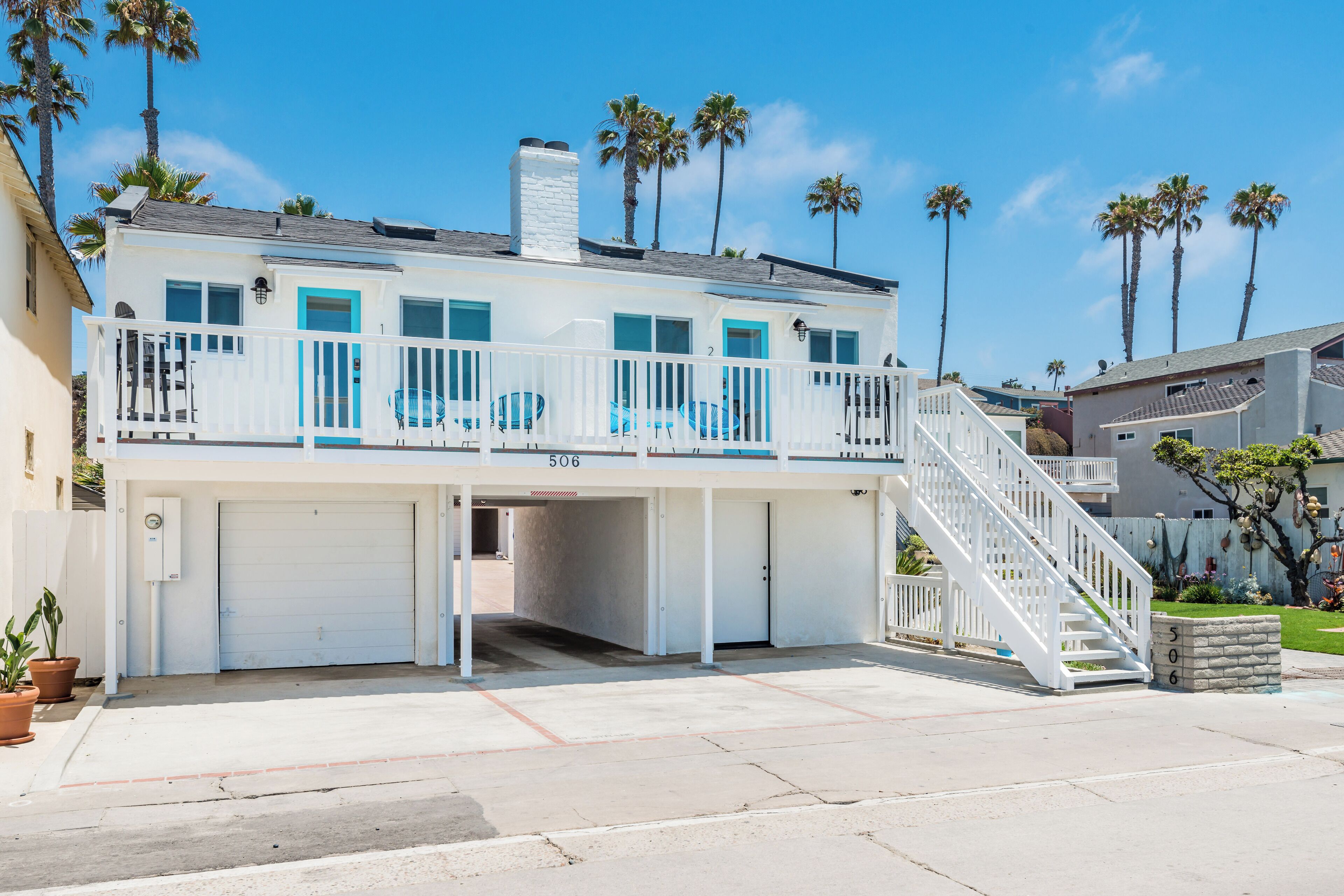 A two-story building with a white exterior, a balcony with blue railings, and a white staircase leading to the upper level.