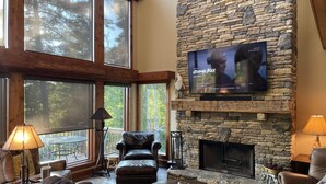 A cozy living room with a stone fireplace, leather furniture, and a TV mounted on the wall. - Private MNT Escape close to DuPont, Pisgah Forest, Brevard, Hendersonville. (Hendersonville)