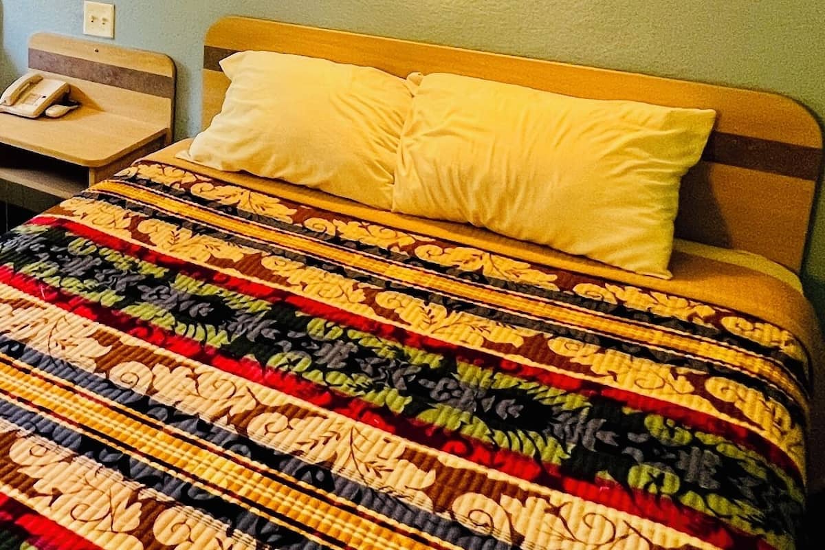 A hotel room with a bed, a nightstand with a telephone, and a wall-mounted light fixture.