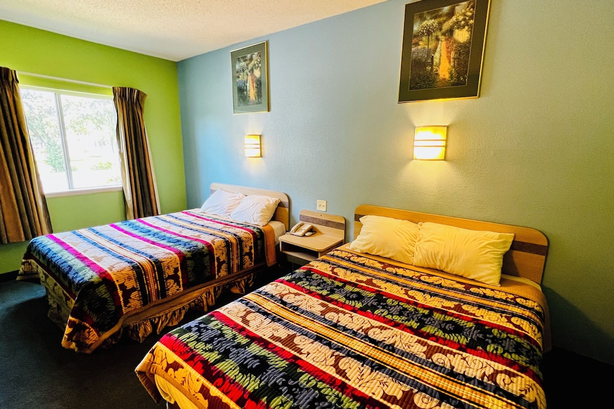 A hotel room with two beds, a window with curtains, and two wall-mounted lights.