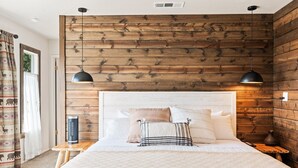 A bedroom with a wooden wall panel, a bed with white bedding, two bedside lamps, and a nightstand with a lamp. - Mountain Retreat on 5 acres with nature views, deck, hot tub, EV charging (Mariposa)