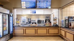 A cafe with a menu board, a coffee machine, a refrigerator with beverages, and a display of pastries.