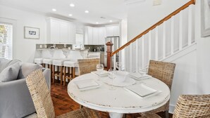 A modern kitchen with white cabinets, a stainless steel refrigerator, and a dining area with a round table and wicker chairs. - 30A Beach House - Beach Bikin (Panama City Beach)