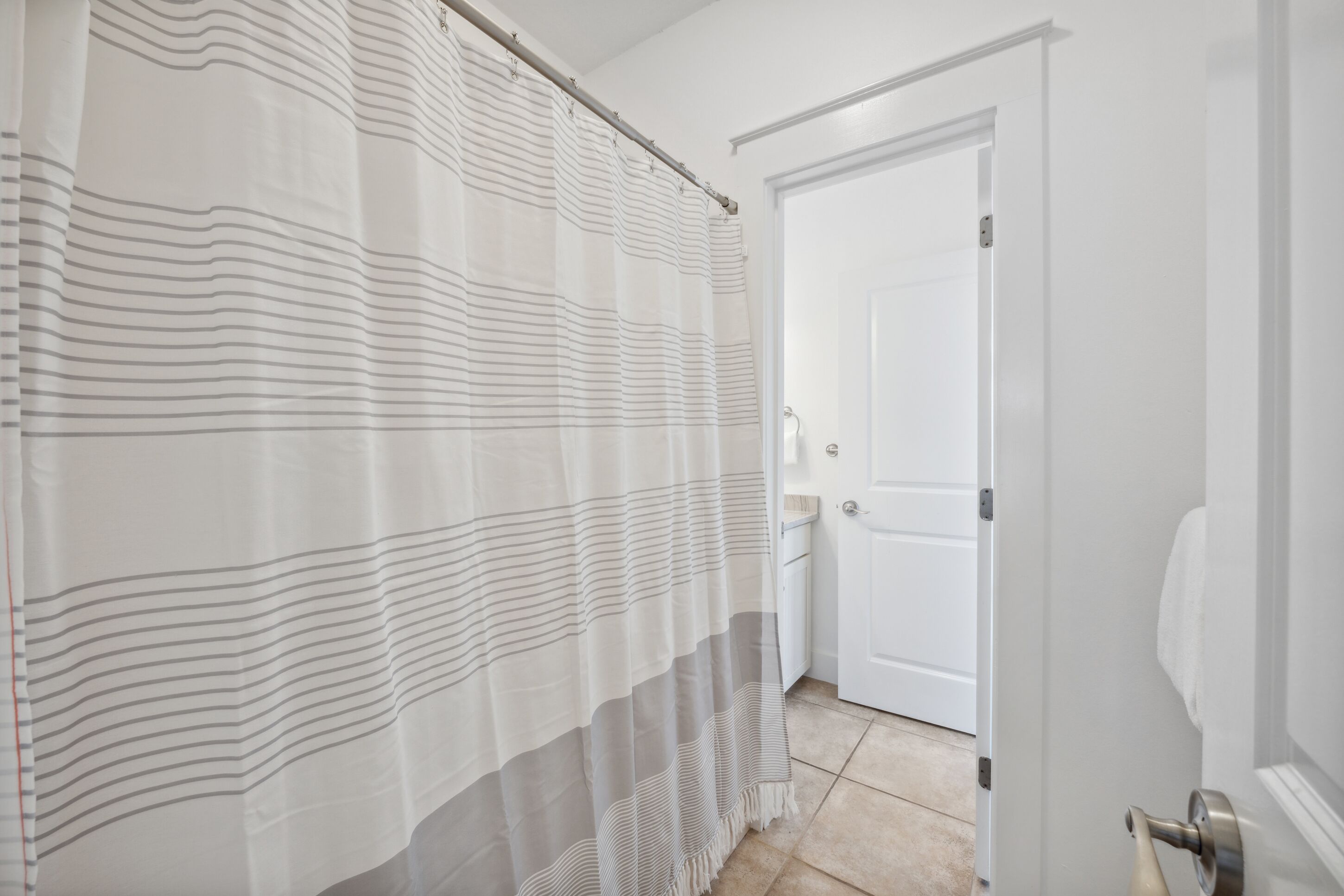 Ein Badezimmer mit gestreifter Duschvorhang, einer weißen Tür und einem Handtuchspender.
