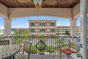 A balcony with a wooden table and chairs, a view of a building with green shutters, and a clear sky. - 30A Beach House - Beach Bikin (Panama City Beach)