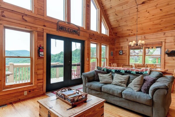 A wooden cabin interior with a couch, a coffee table, and a 'WELCOME' sign.