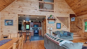 L’intérieur chaleureux d’un chalet comprend un coin repas, une cuisine et un salon avec un canapé et un escalier.