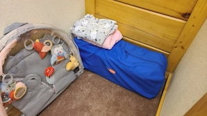 Zona de juegos para niños con una cama pequeña, un contenedor de almacenamiento con juguetes y una manta azul en el suelo.