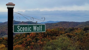 Una señal de calle que dice 'Scenic Wolf' frente a follaje otoñal y montañas.