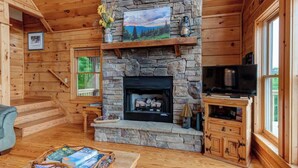 Interior acogedor de una cabaña con chimenea de piedra, paredes de madera, un televisor y una estantería.