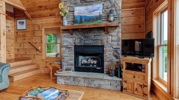 Interior acogedor de una cabaña con chimenea de piedra, paredes de madera, un televisor y una estantería.