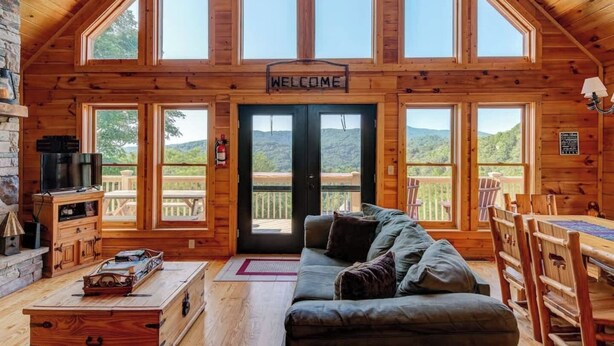 Una cabaña de troncos con un letrero que dice 'WELCOME', un sofá, un televisor y una mesa de comedor.