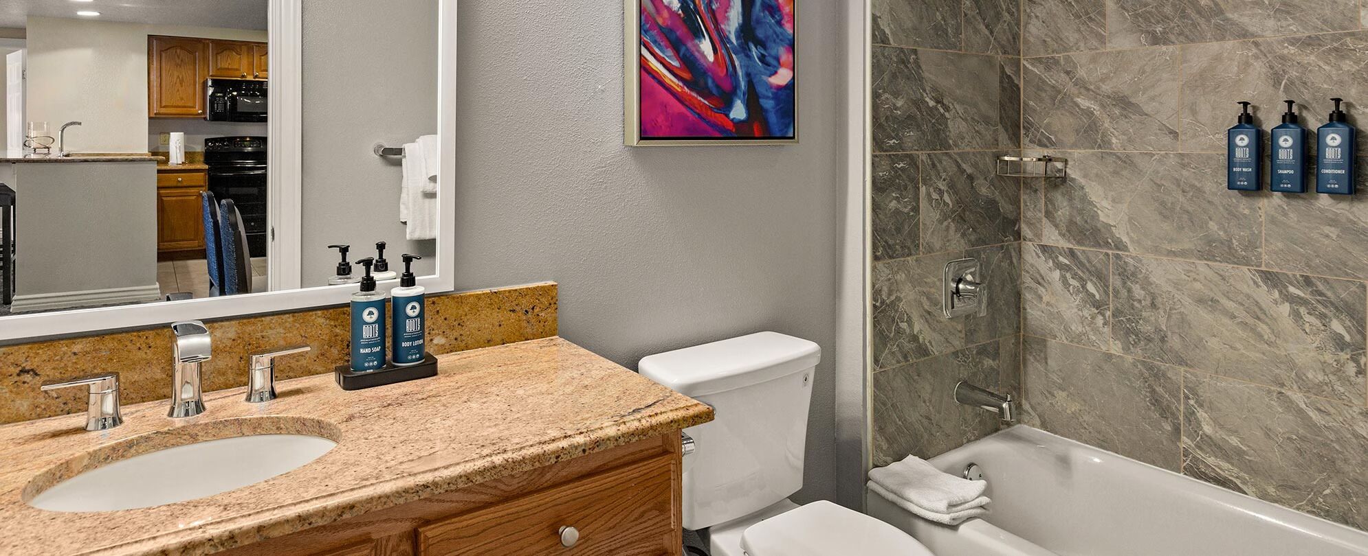 Een badkamer met een granieten aanrechtblad, een wit toilet, een douche met marmeren wanden en een grote spiegel.