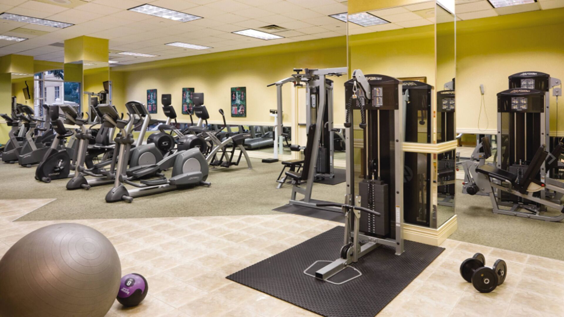 Une salle de sport équipée de divers appareils d’exercice, notamment des tapis de course, des appareils elliptiques et des appareils de musculation.