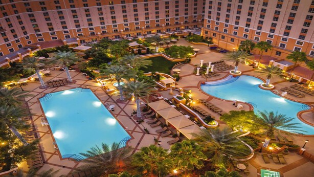 Un hotel con varias piscinas, palmeras y zonas de estar al aire libre.
