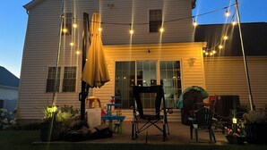 A house with a patio area featuring outdoor furniture, string lights, and a covered seating area. - ☘️ 10 mins to Notre Dame, 4 Bedrooms, Garage Park, Restaurants Close. Go Irish!☘️ (South Bend)