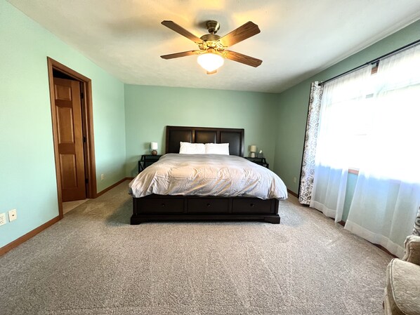 A bedroom with a bed, a ceiling fan, a nightstand, and a window with curtains.