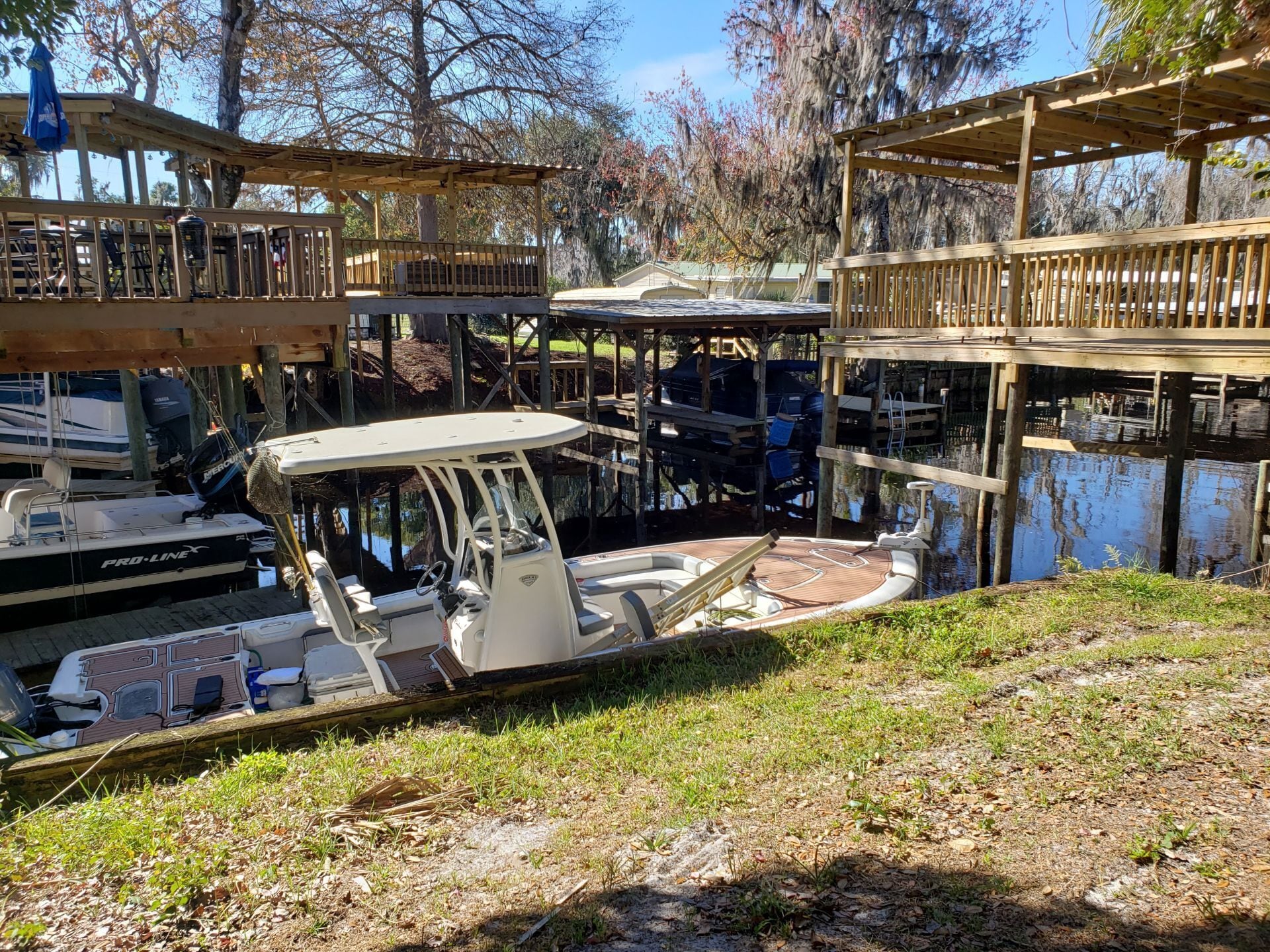 A docked boat with a cabin, surrounded by wooden structures and trees.