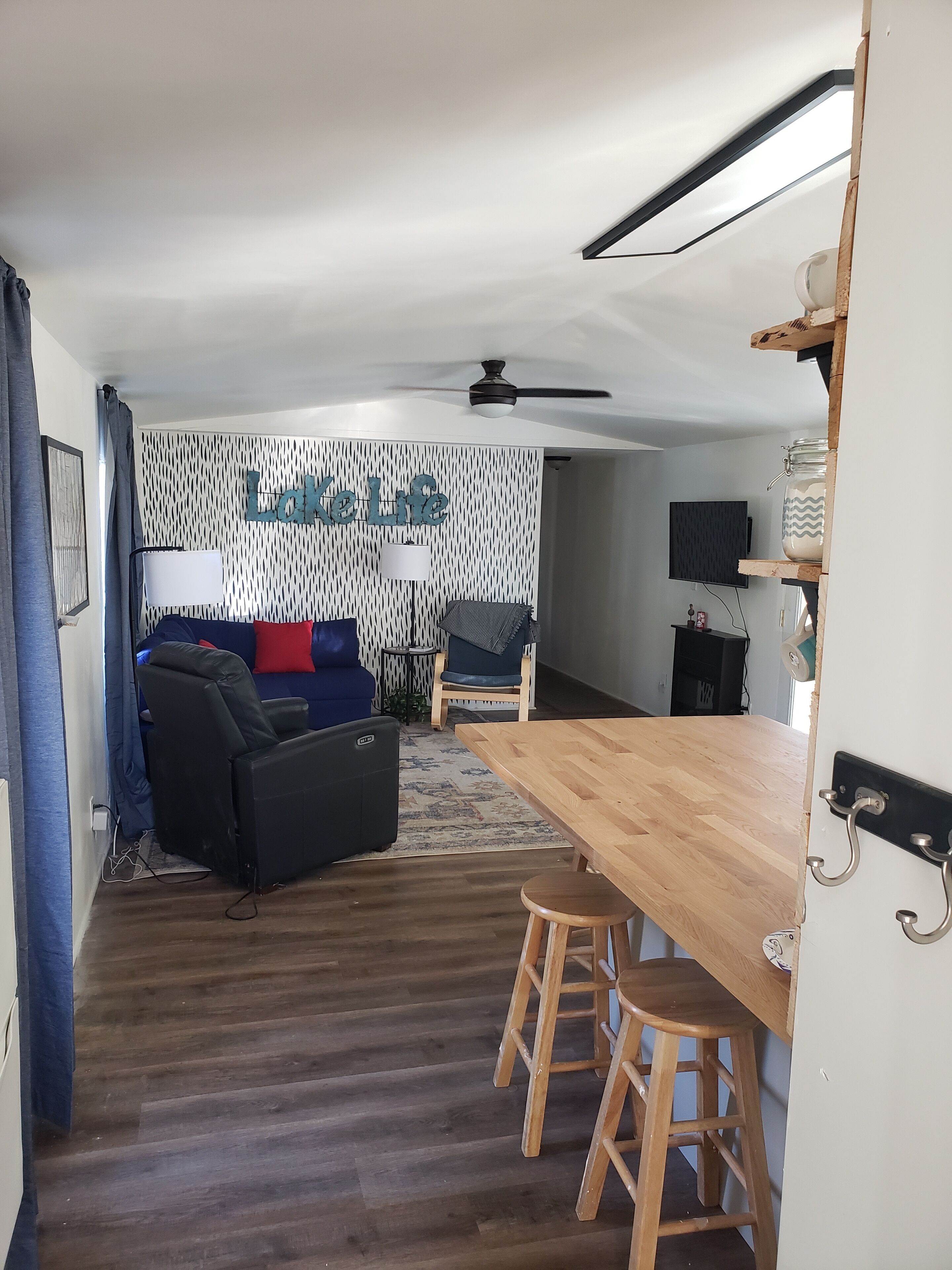 Una sala de estar moderna con sofá, una mesa de centro y un televisor. Hay una mesa de comedor de madera con taburetes.