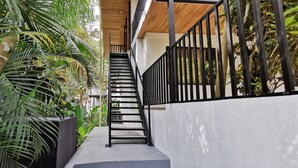 A modern staircase with black railings, surrounded by lush greenery and a white wall.