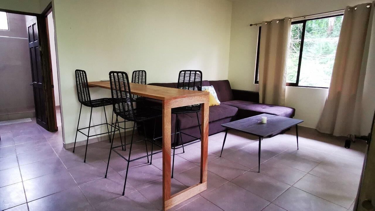 Un comedor con una mesa de madera y cuatro sillas, un sofá y una mesita con una vela.