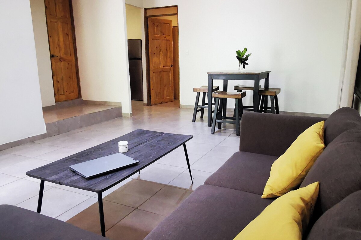 Uma sala de estar com sofá, mesa de centro e uma área de jantar com cadeiras e mesa.