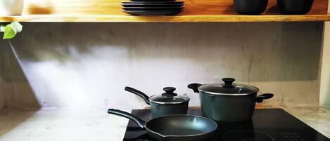 A kitchen with a stove, a frying pan, a pot, and a stack of black bowls on a wooden shelf.