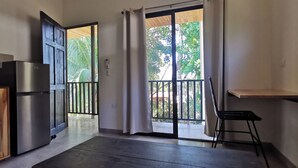 A room with a sliding glass door leading to a balcony, a refrigerator, and a small table with a chair.