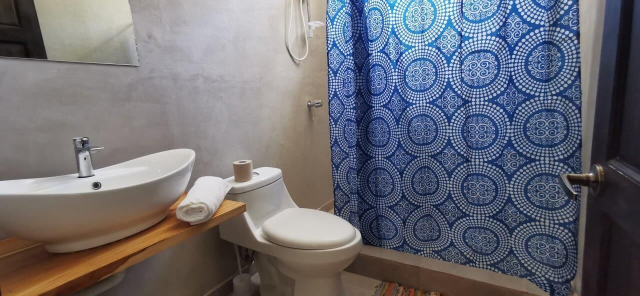 Un baño con lavamanos blanco, inodoro y cortina de ducha con estampado azul.