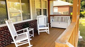 A covered porch with two rocking chairs and a bench, wooden deck, and a brick wall. - Cozy ranch, minutes from both historic downtown Savannah and Tybee Beaches. (Savannah)