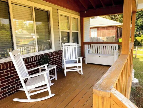 A covered porch with two rocking chairs and a bench, wooden deck, and a brick wall. - Cozy ranch, minutes from both historic downtown Savannah and Tybee Beaches. (Savannah)