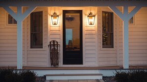 A house with a porch, two lit lanterns, and a black door. - Ann Riley Farmhouse Yuba Vineyards (Williamsburg)