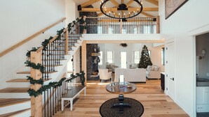 A spacious interior with a wooden staircase, a chandelier, a Christmas tree, and a cozy seating area. - Ann Riley Farmhouse Yuba Vineyards (Williamsburg)