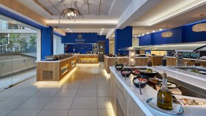 Una cocina de hotel moderna con una decoración azul y blanca, que incluye una isla central con diversos alimentos y una botella de aceite de oliva en la encimera.