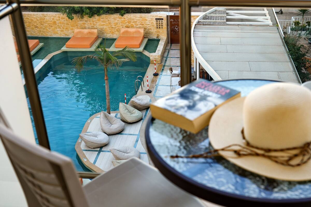 A poolside view with lounge chairs, a palm tree, and a book on a table.